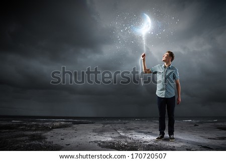 Young man holding moon balloon against dark background