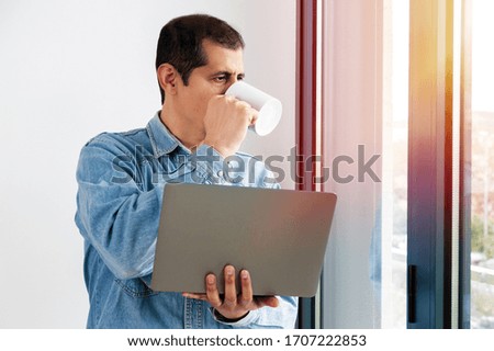 Cropped shot of a businessman using his laptop while drinking coffee and looking out of the office window