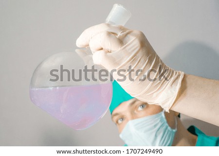 A doctor in a medical mask and latex gloves looks at the tests in a flask.