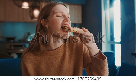 Close up view of happy hungry pretty blondehair girl sitting on blue sofa at home and eating tasty pizza, enjoying and smiling. Royalty-Free Stock Photo #1707256495