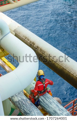 Working at height. A top view of abseiler wearing Personal Protective Equipment (PPE) sitting on the pipeline for touch up painting activities.