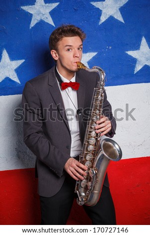 Studio portrait of young cool man with saxophone on American flag background.