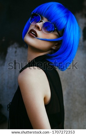 Woman with short electric blue hair and sunglasses posing on urban wall background. Concept of future and cosmos. 