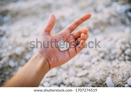 White heart shape stone lying on palm on beach background.