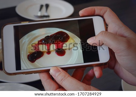 Blogger young woman take picture,which her hand holding phone taking photo of stylish  flat lay blue berry cheese cake  in the cafe and restaurant