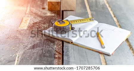 draw prepared wood products in a workbook in a joinery. tape measure, pencil and notebook on the table with chainsaw Royalty-Free Stock Photo #1707285706