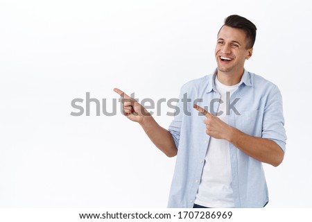 Portrait of handsome happy caucasian man with stylish haircut, laughing and smiling pleased, seeing something good, pointing and looking left at blank space for your product, company banner or promo