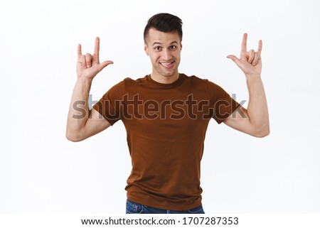 Rock on, portrait of cheerful happy caucasian man enjoying awesome festival or concert, praying, show tongue smiling and make heavy-metal signs, standing white background having fun