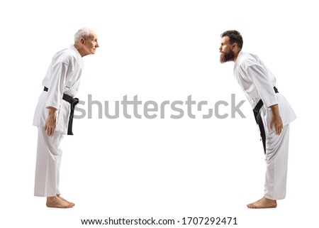 Full length profile shot of karate masters with black belts bowing isolated on white background