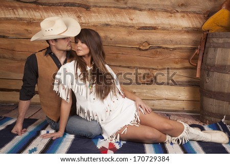 A cowboy and Indian woman are sitting and ready to kiss.