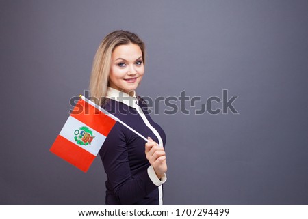 Immigration and the study of foreign languages, concept. A young smiling woman with a Peru flag in her hand. Girl waving a Peruvian flag on a gray background