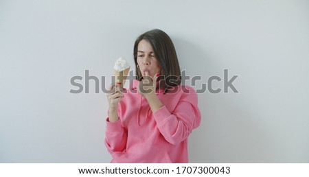 Young woman eating ice cream over white wall background. Girl in red sungrasses enjoying sweet yummy