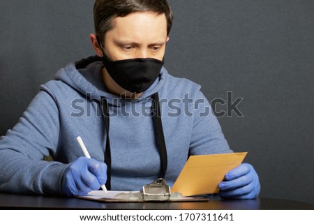 Delivery of correspondence during the period of self-isolation. A man in rubber gloves and a mask signs a delivery form. In the other hand holds a letter.