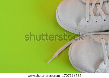 Pair of white shoes on bright green background. Trendy summer color. Copy space and cool hipster color. A pair of white sneakers on vivid green background. White sports sneakers on bright green color.