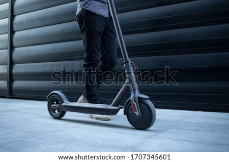 Electric scooter commuting vehicle. Eco friendly transportation. Unrecognizable modern person walking by his electric scooter. Modern way of environmental transportation. Royalty-Free Stock Photo #1707345601