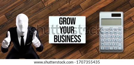 lightbox with message GROW YOUR BUSINESS and person in morphsuit with thumbs up gesture on wooden background