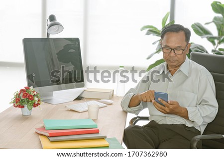 A senior asian man using smartphone on work desk at home