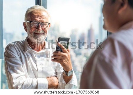 Picture of two business man discussing business and seem like an agreement is made. The young man is wearing white shirt with black tie. The older man is wearing black suit. They meet in hotel lobby.