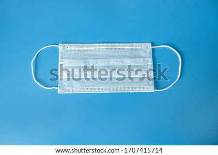 A typical 3-layer medical surgical mask to cover the mouth and nose on a blue background. Concept of protection against bacteria and coronavirus