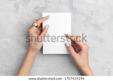 Manicured woman's hands holding postcard on grey concrete background. Plain call-card mock up template.

