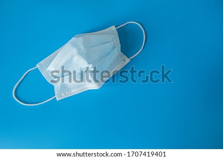 A typical 3-layer medical surgical mask to cover the mouth and nose on a blue background. Concept of protection against bacteria and coronavirus
