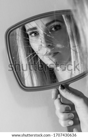 Black and white of Caucasian female's reflection in handheld broken mirror.  Solemn look.