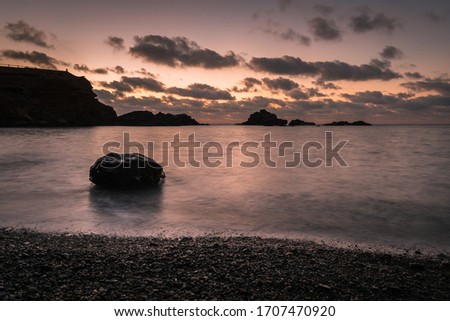 A stunning and colorful seascape  from a beautiful pebble beach at sunrise with some rocks in the background, Cabo de Palos, Murcia, Spain