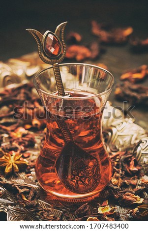 Glass cup of red tea with Hibiscus (Karkade) in Turkish style, leaves scattered on  table, dark background, selective focus with shallow depth of field