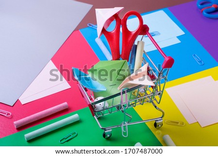 Stationery and multicolored paper origami toys in a little shopping cart against the geometric background