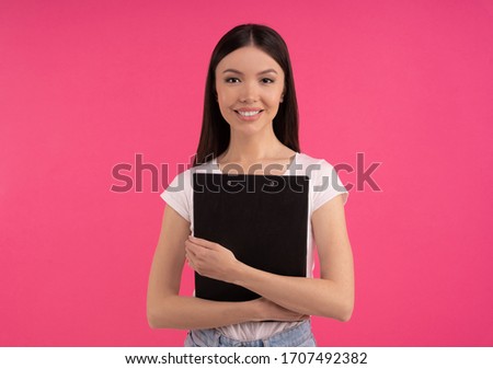 Studio shot of happy young Asian woman has tender smile, student with charming expression, wears casual white t shirt, has natural beauty, isolated on pink wall. Study and emotions concept.