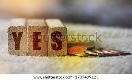 The word Yes written on wooden blocks with coins besides. Business financing positive answr sponsorship, motivation and education concept.