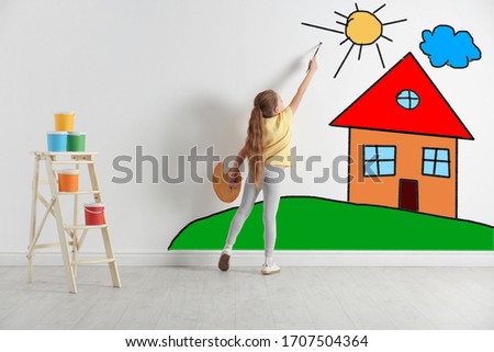 Cute child drawing landscape with house on white wall indoors