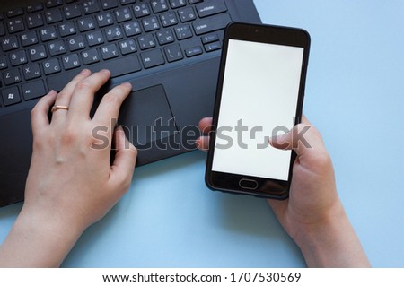 man works at a laptop and holds a phone in his hand flatly.the problem of concentration at work while working from home.man distracted by phone while working from home on laptop.
