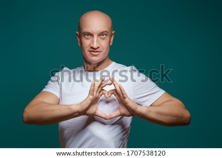 Portrait of a bald man smiling and holding hands in the shape of a heart, on a blue background . The concept of romance.