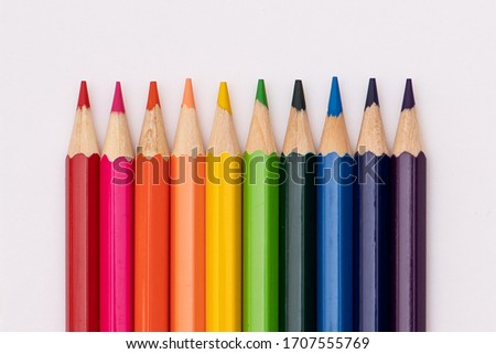 pencils of red, orange, yellow, green, azure, blue, and purple lie vertically on a white background in the shape of a rainbow