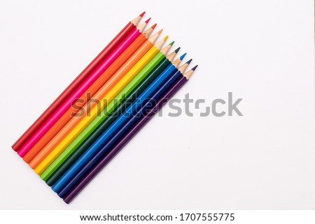 pencils of red, orange, yellow, green, azure, blue, and purple lie vertically on a white background in the shape of a rainbow