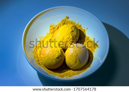 We paint chicken eggs in culinary spices of turmeric, a plate on a blue background