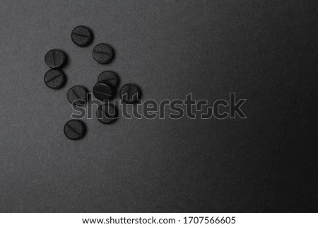 Close up of rough black round tablets, made of absorbent carbon in a light spot of dark grey surface. Top angle view, there is space for advertising and sign