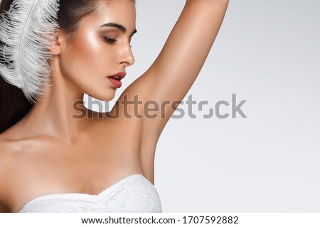 Portrait of attractive Caucasian woman with raised hand. beautiful young girl holds feather in hands and looks at armpit. Smooth clean skin of the face and body. concept care, epilation armpit Royalty-Free Stock Photo #1707592882