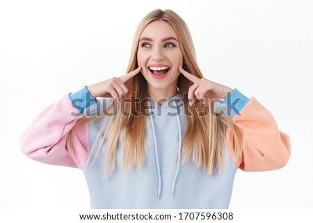 Beauty, lifestyle and fashion concept. Upbeat good-looking blond girl poking her cheeks and smiling, looking away with joyful, happy emotion, promote skincare cosmetics or makeup