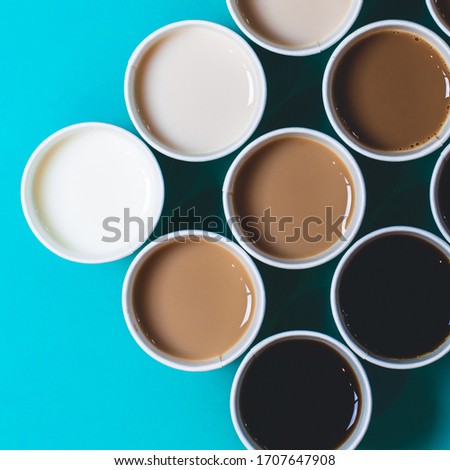 Minimal top view image of coffee in paper cups with different mounts of milk, creating a gradient. Turquoise background. Flat lay 