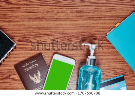Top view picture of Thailand passport with smartphone,alcohol gel,credit card and notebook paper on wood table background.