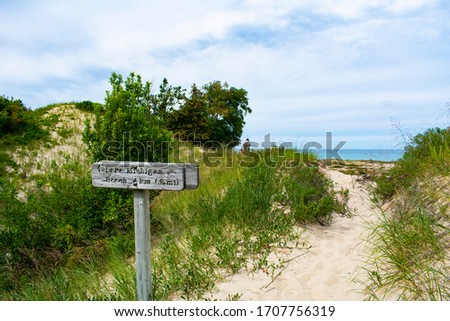 Old weathered sign on Old Indian Trail in Sleeping Bear Dunes National Lakeshore with hikers in background. View of Lake Michigan and South Manitou Island. Bright summer day.