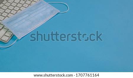 Medical face mask on top of keyboard. B;ue background. Top view. Copy space.