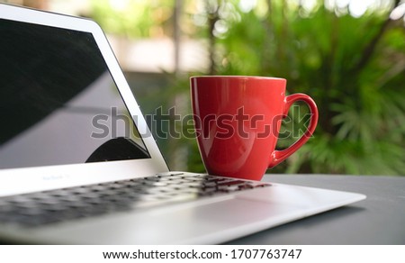 Computer laptop with offee in red cup with green nature background. Work remotely or from home. Selected focus. Copy space.