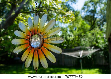Sunflower decoration hanging from porch awning on bright and sunny summer day. Yellow and orange pedals with diamond reflective center. 