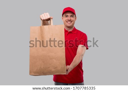 Delivery Man With Paper Bag in Hands. Red Uniform Delivery Boy. Home Food Delivery. Paper Bag Close Up Royalty-Free Stock Photo #1707785335