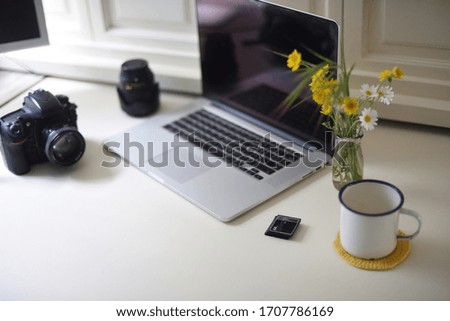 Home photography workstation with camera, coffee and flowers.