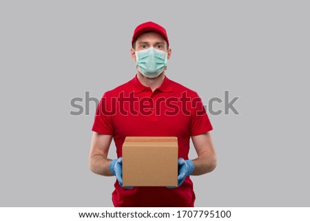 Delivery Man Wearing Medical Mask and Gloves with Box in Hands. Red Tshirt Delivery Boy. Home Delivery. Quarantine Hero. Man Smiling Royalty-Free Stock Photo #1707795100