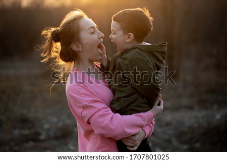 Close up of a lovely mother and her son having fun outdoor. Little cute kid holded by her mom in the arms which is laughing against sunset. Mother's day concept.